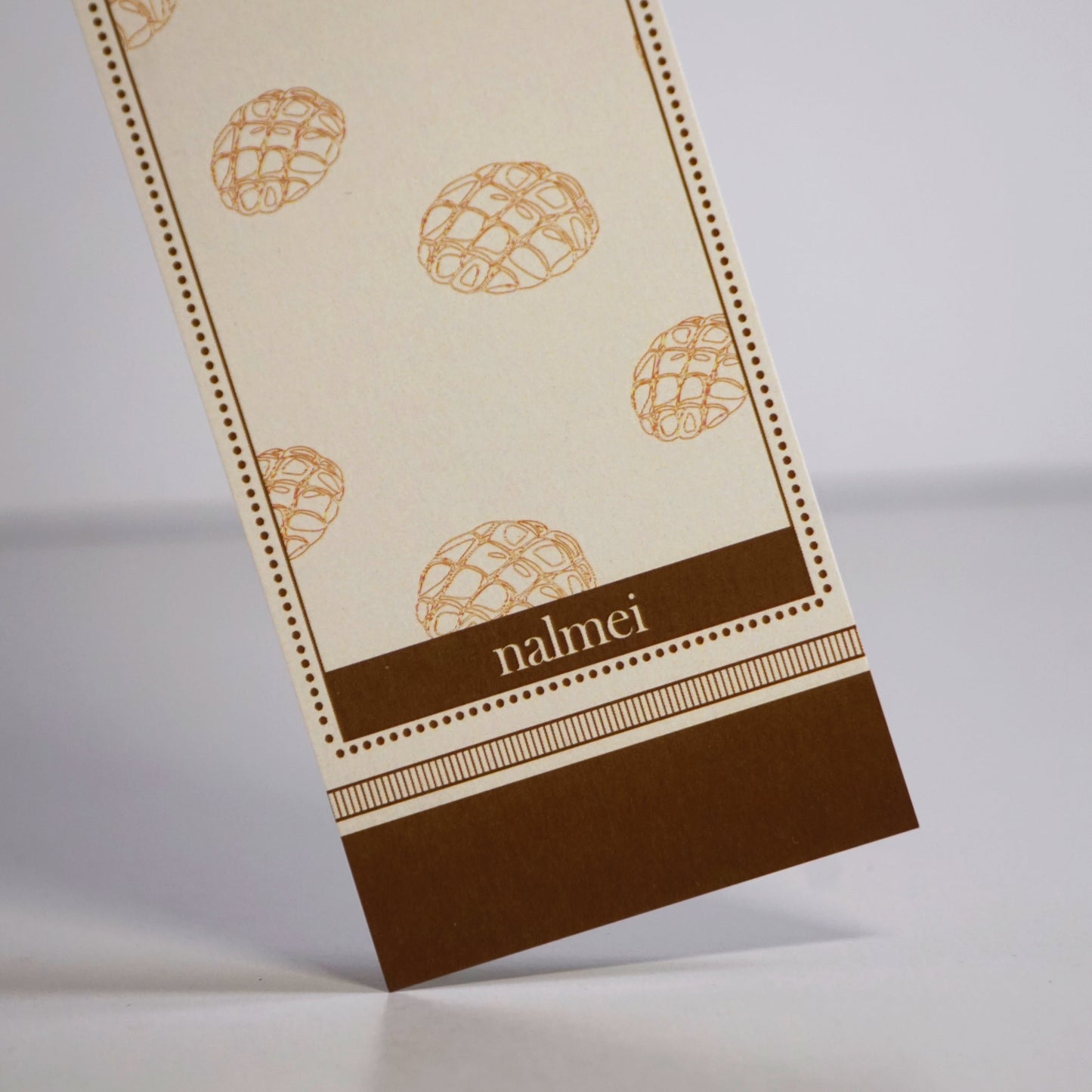 Close up of a brown and beige large bookmark with melonpan bread illustration outlined | Nalmei