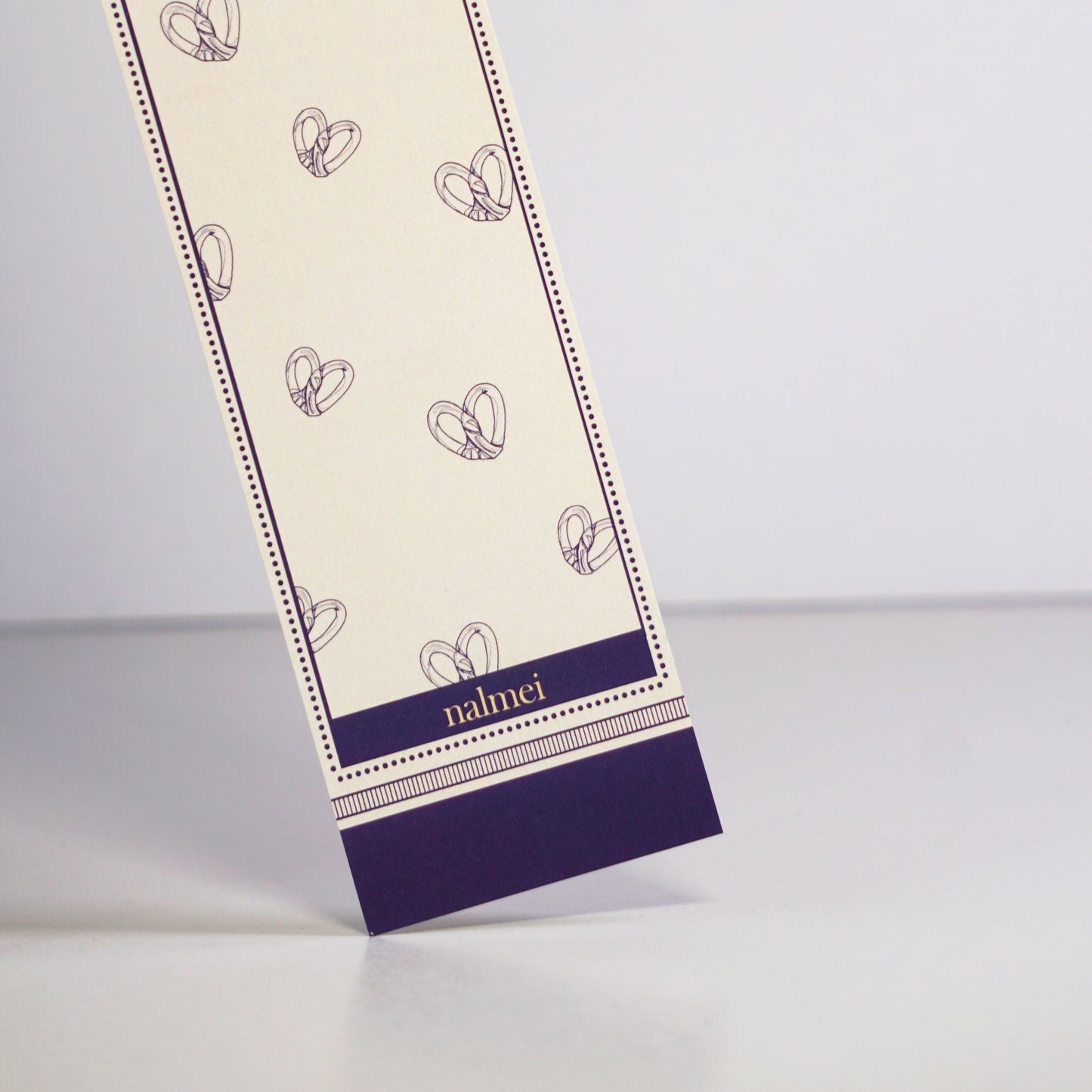 Close up of a purple and beige large bookmark with pretzel bread illustration outlined | Nalmei
