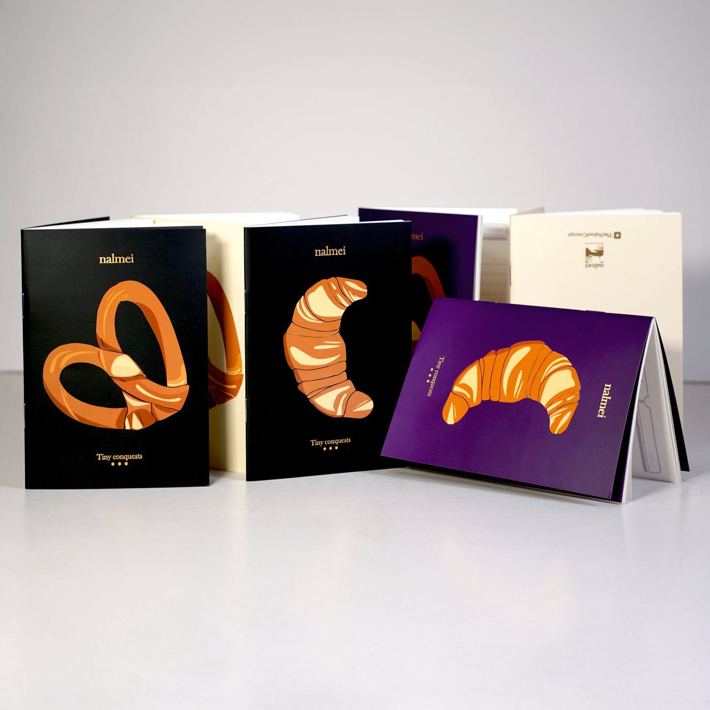 A set of 6 pocket notebooks with Black, Beige and Purple Croissants and Pretzels illustrations | Nalmei