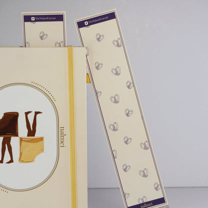 A purple and beige large bookmark with pretzel bread illustration outlined leaning on a quotes journal| Nalmei