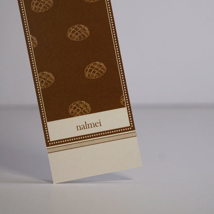 Close up of a brown and beige large bookmark with melonpan bread illustrations | Nalmei